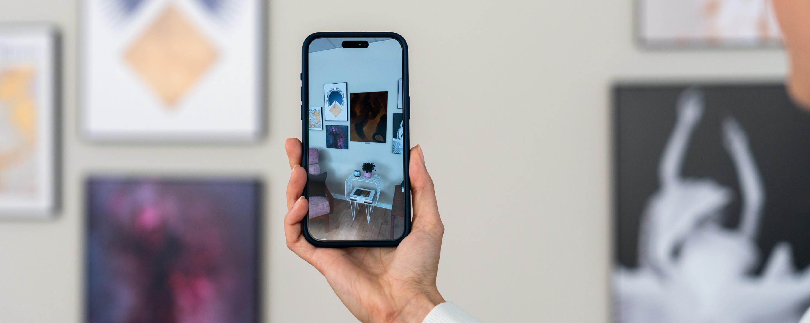 Hand holding a smartphone with an AR view of a gallery wall featuring modern art posters