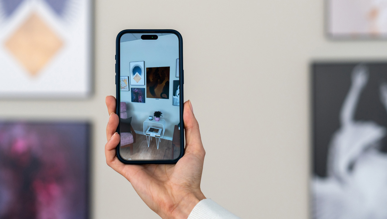 Hand holding a smartphone with an AR view of a gallery wall featuring modern art posters