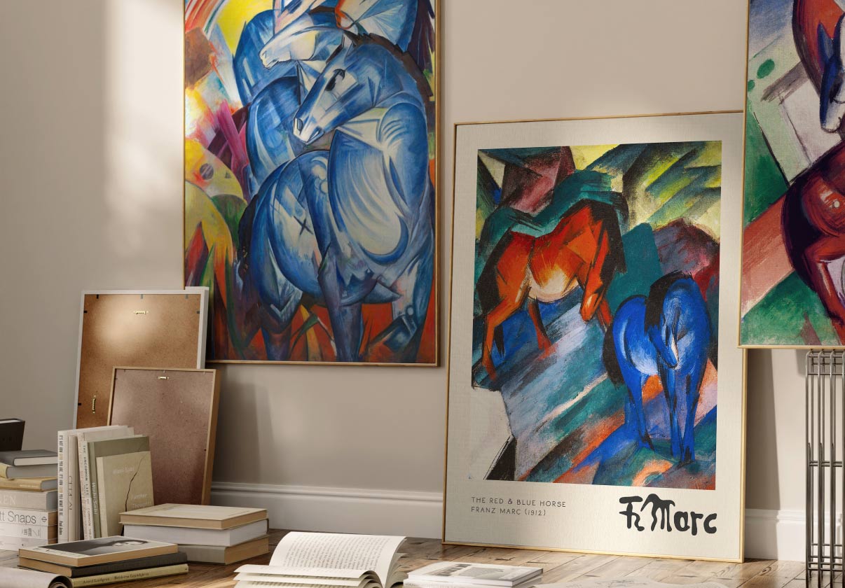 Zwei gerahmte Wandbilder der Bewegung „Der Blaue Reiter“ stehen an einer Wand, davor liegen Bücher auf dem Boden.