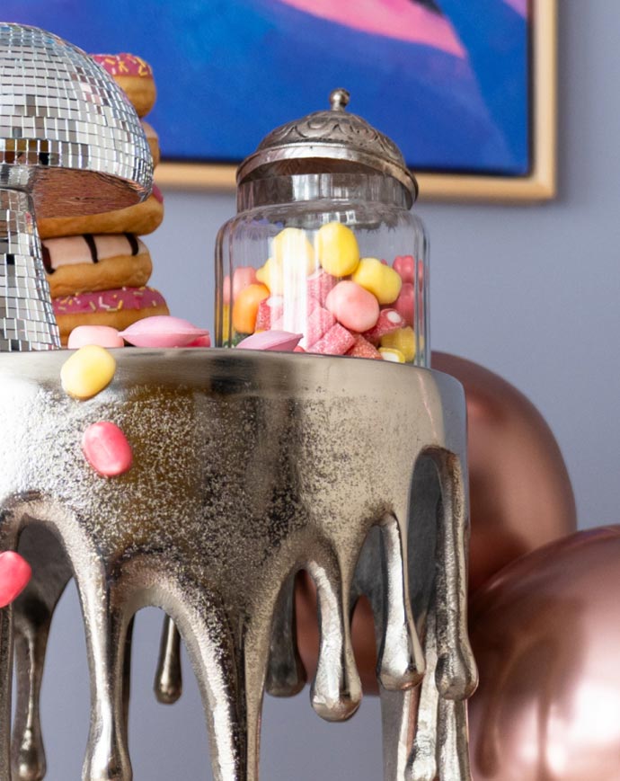 Close-up of a decorative table with a glass jar full of colourful sweets, disco ball and doughnuts in the background