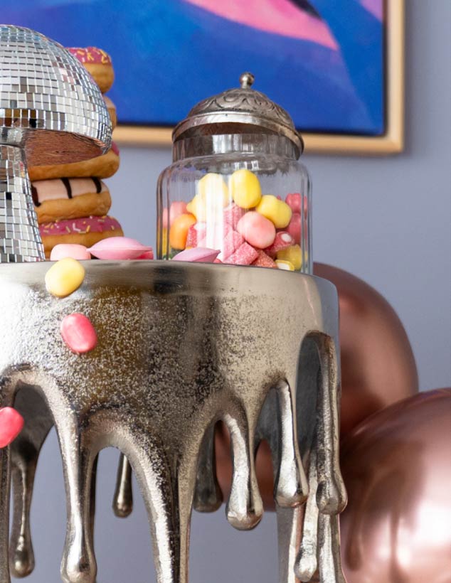 Close-up of a decorative table with a glass jar full of colourful sweets, disco ball and doughnuts in the background