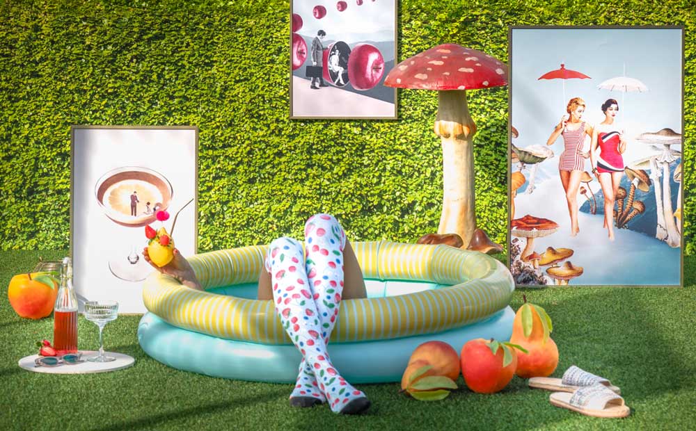 Creative summer scene with a paddling pool, cocktail, vibrant art prints and decorative mushrooms on a grassy lawn