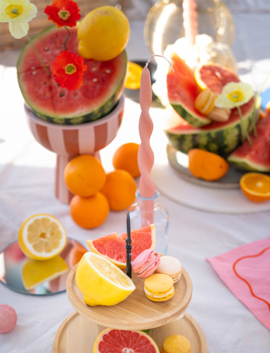 Summery table decor with lemons, watermelons, macarons and colourful flowers on a tiered stand
