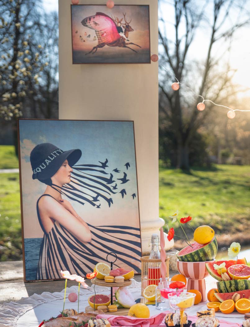Outdoor summer picnic with art prints, fresh citrus fruits, watermelons, macarons and flower arrangements on a blanket in the park